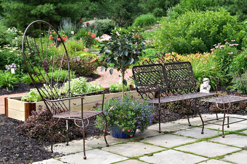 Jardin paysager avec salon de jardin en fer forgé noir sur dallage pierre naturelle avec joints enherbés