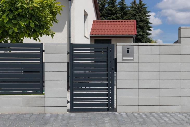 Façade résidentielle avec portail coulissant et portillon en métal brun foncé, piliers en briques beiges, éclairage LED intégré