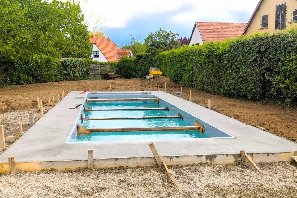 Un ouvrier en casquette bleue plante un arbre dans une fosse creus&eacute;e dans le jardin